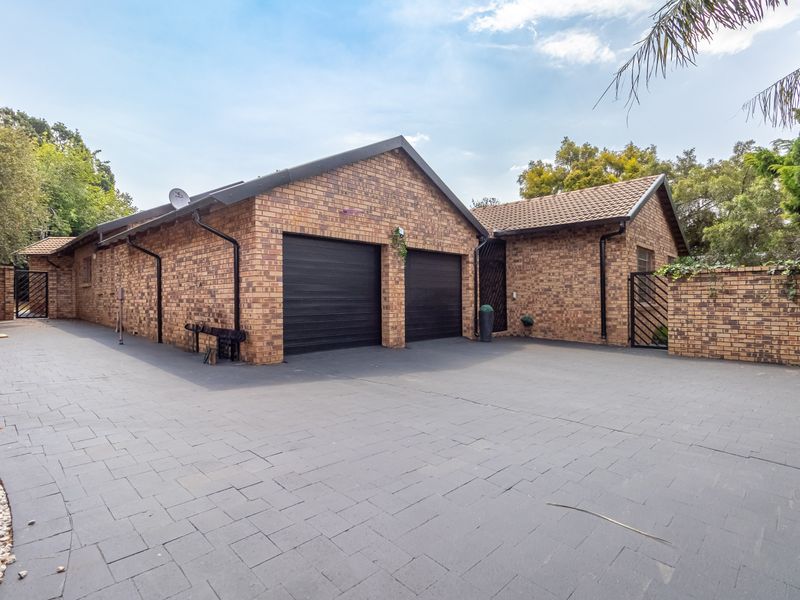 A well-maintained brick-faced house exterior featuring a spacious paved driveway and a double garage with modern black roller doors.