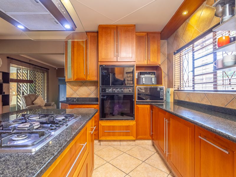 A well-maintained kitchen featuring warm wooden cabinetry, granite countertops, a gas hob with extractor, and a built-in double oven.