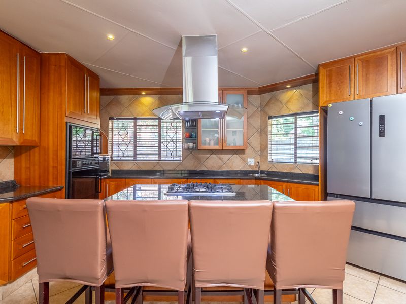 A well-appointed kitchen featuring warm wooden cabinetry, granite countertops, a central island with a gas hob, and a stainless steel extractor fan.