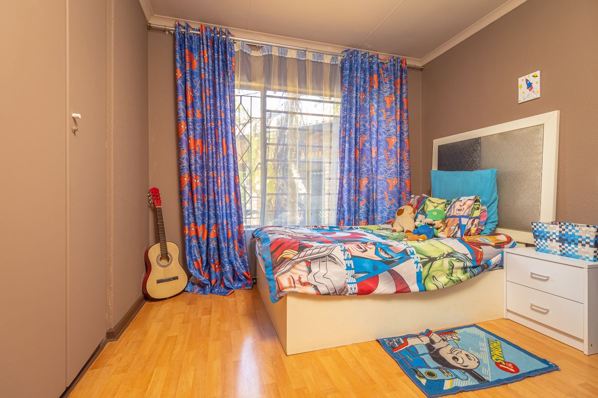 A bedroom featuring laminate flooring, a built-in cupboard, and a window fitted with a security gate.