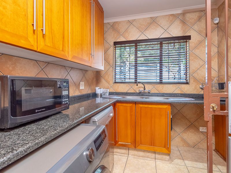A functional scullery featuring timber cabinetry, granite countertops, a double stainless steel sink, and tiled splashbacks, providing ample space for laundry and prep.
