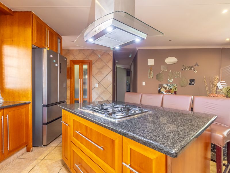 A functional kitchen featuring a central island with a gas hob, granite countertops, and warm-toned wooden cabinetry with ample storage space.