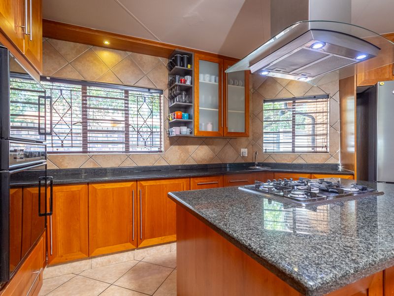 Well-appointed kitchen featuring granite countertops, wooden cabinetry, a central island with a gas hob, and an integrated extractor fan.