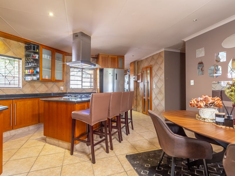 Open-plan kitchen and dining area featuring warm wooden cabinetry, granite countertops, a central island with a gas hob, and neutral tiled flooring throughout.