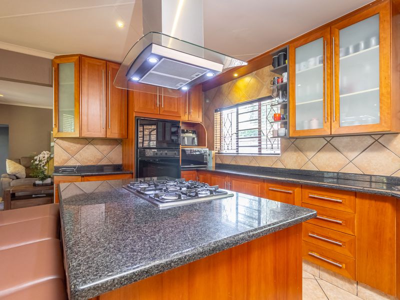 A well-appointed kitchen featuring granite countertops, wooden cabinetry, a central island with a gas hob, and a modern extractor fan.