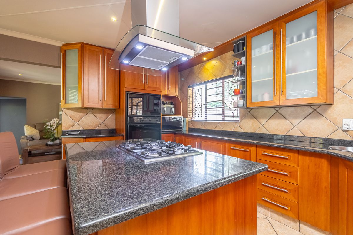 A well-appointed kitchen featuring granite countertops, wooden cabinetry, a central island with a gas hob, and a modern extractor fan.