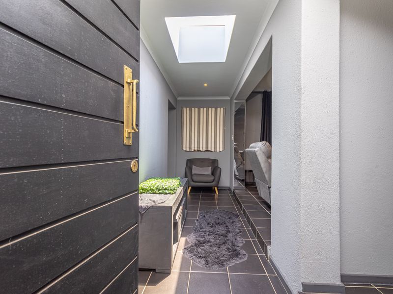 A modern entrance hall featuring dark tiled flooring, a large solid timber front door with brass hardware, and a bright overhead skylight.
