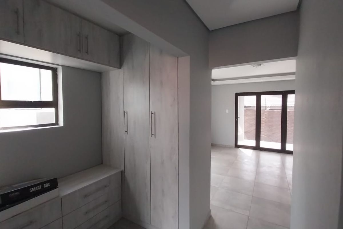 A bright bedroom featuring built-in cabinetry with light wood-grain finish, tiled flooring, and large sliding doors leading to an outdoor area.