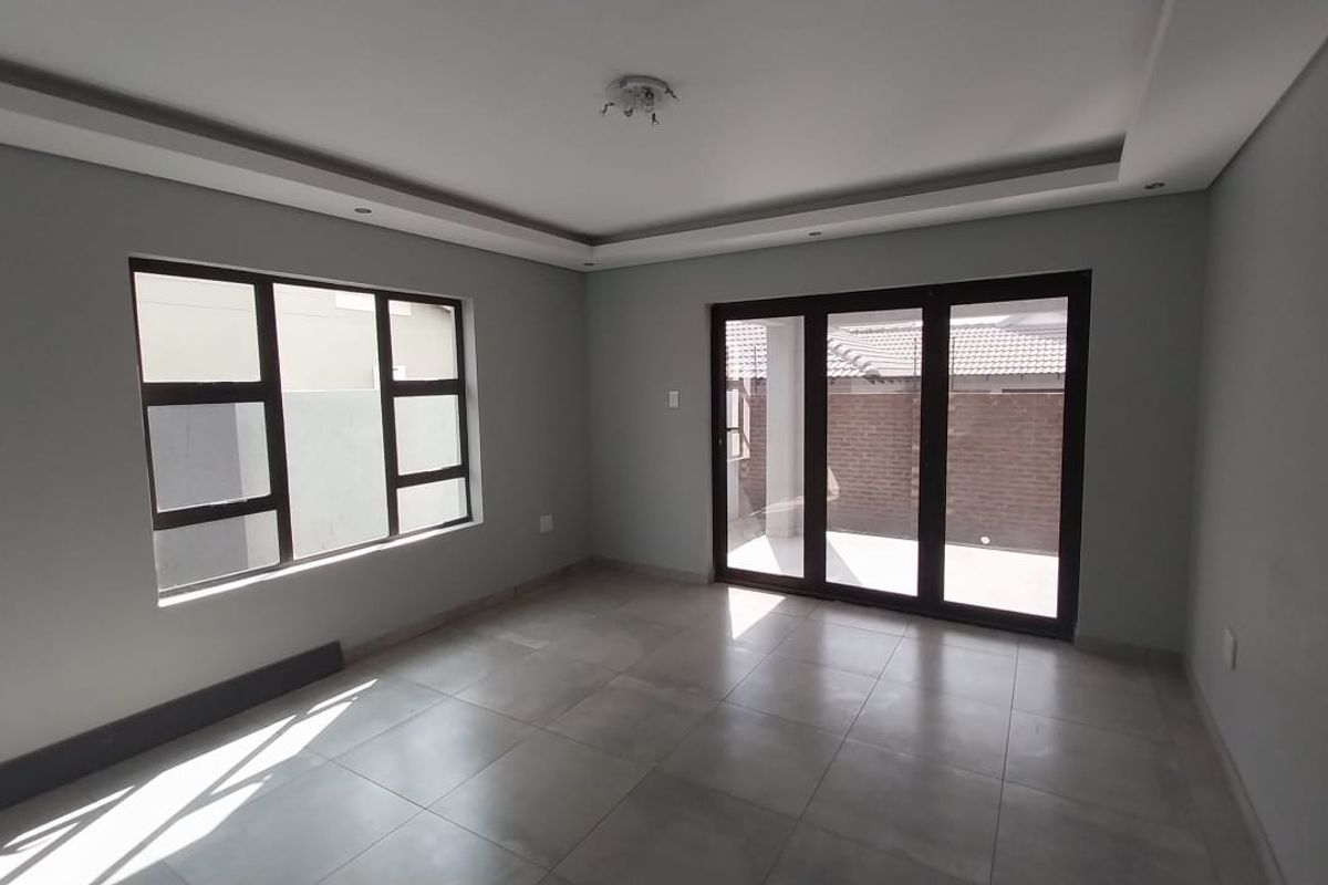 A bright, empty living room featuring modern grey floor tiles, recessed ceiling lighting, and large sliding glass doors leading to an outdoor patio area.