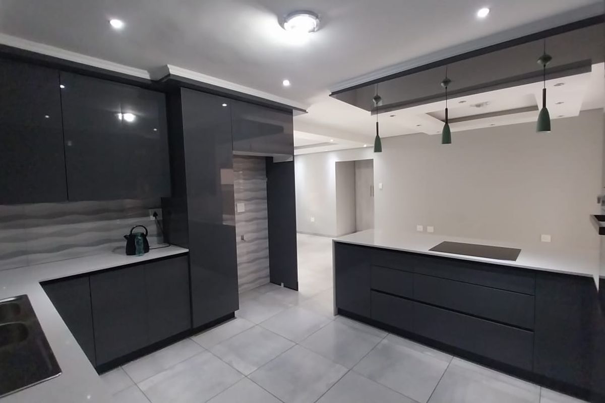 Modern kitchen featuring high-gloss grey cabinetry, stone countertops, a central island with an integrated cooktop, and recessed ceiling lighting.