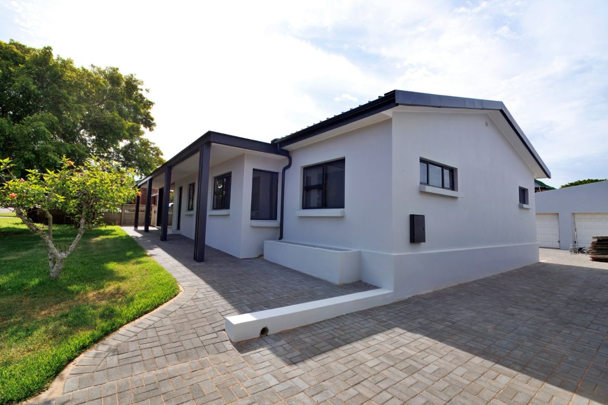 A well-maintained exterior rear view of the house featuring a paved patio area, covered walkway, and neat garden landscaping.