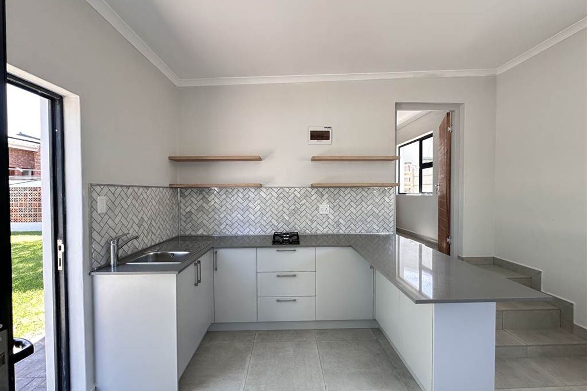 Modern kitchen featuring light grey cabinetry, stone countertops, herringbone tile backsplash, floating timber shelves, and a built-in gas hob.