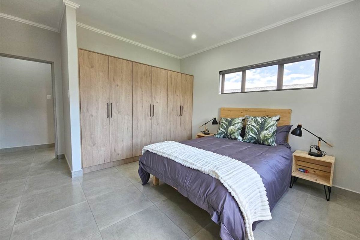 A well-maintained bedroom featuring large built-in wooden wardrobes, neutral floor tiles, and a horizontal window providing natural light.