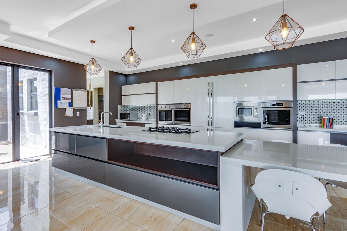 Modern kitchen featuring a large central island with stone countertops, integrated stainless steel appliances, high-gloss cabinetry, and contemporary pendant lighting.