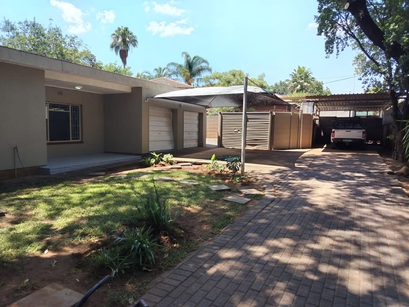 Front exterior view featuring a paved driveway, double garage, shade sail carport, and a landscaped garden area.