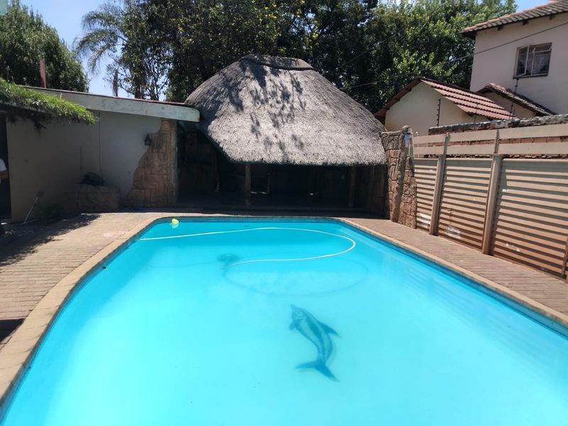 Outdoor swimming pool area featuring a thatched lapa entertainment space, paved surround, and perimeter fencing.