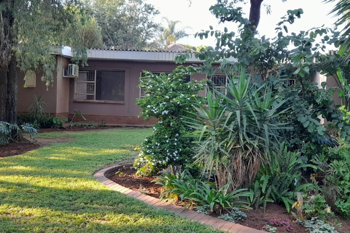 A view of the rear exterior of the house featuring a well-established garden with mature trees and landscaped beds.