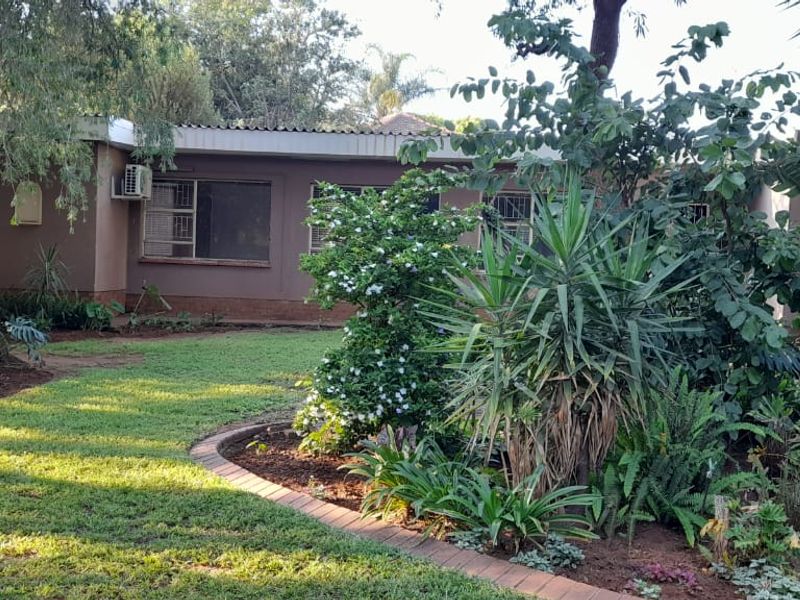 A view of the rear exterior of the house featuring a well-established garden with mature trees and landscaped beds.