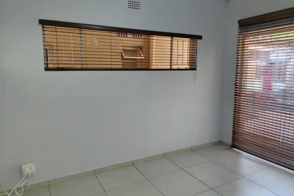 An empty room featuring light-colored floor tiles, horizontal wooden blinds, and a neutral wall finish, suitable for a bedroom or living area.
