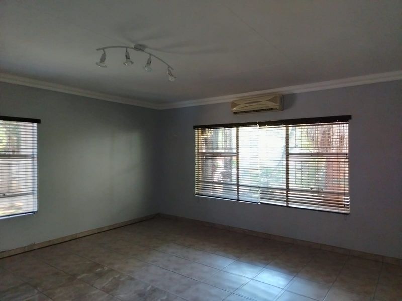 An empty living room featuring tiled flooring, large windows with fitted blinds, and a wall-mounted air conditioning unit.