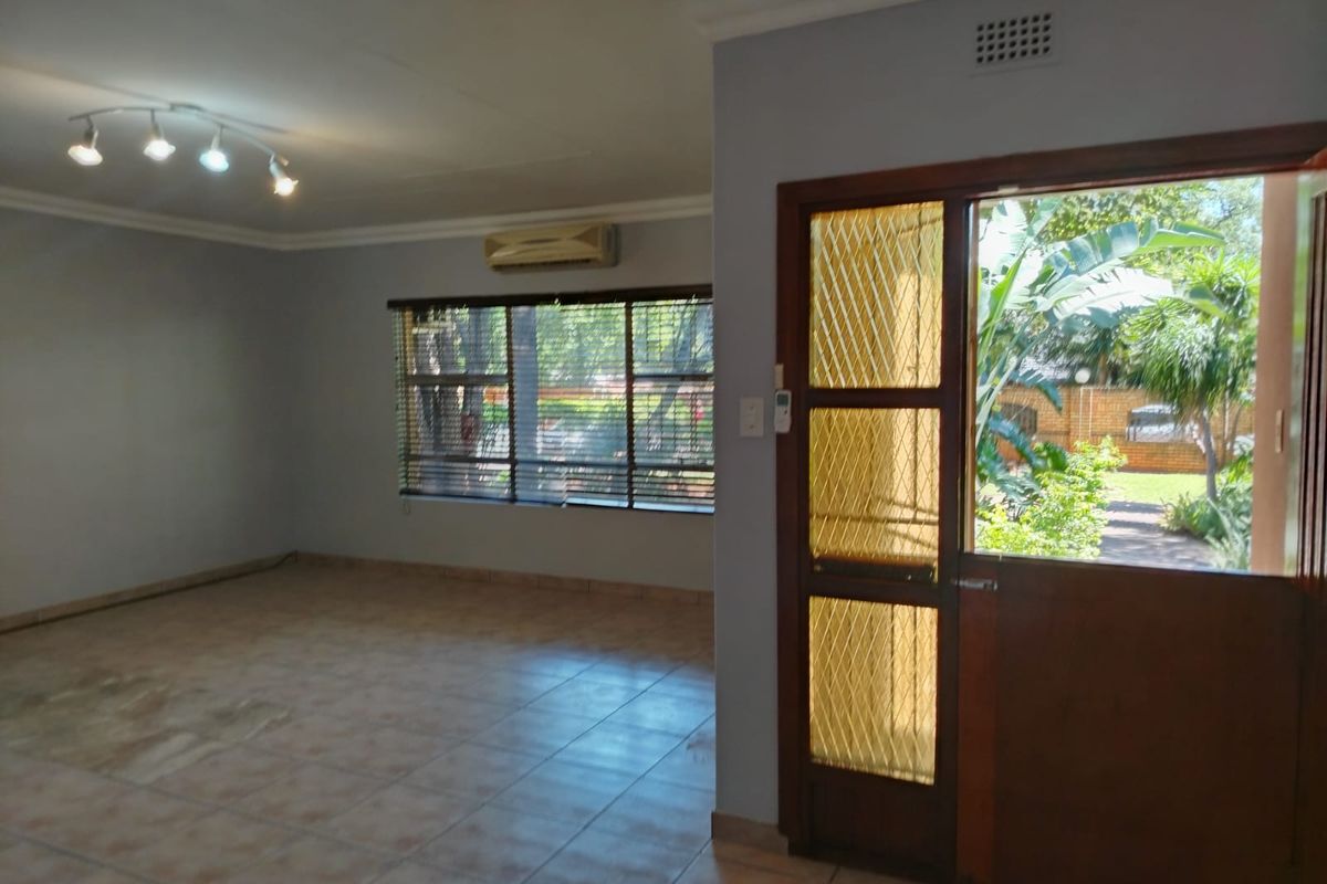 Spacious living area featuring tiled flooring, a wall-mounted air conditioning unit, and a wooden door with security mesh leading to the garden.