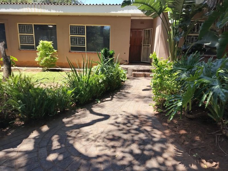Front entrance view featuring a paved walkway leading to the main door, surrounded by established garden landscaping and exterior building facade.