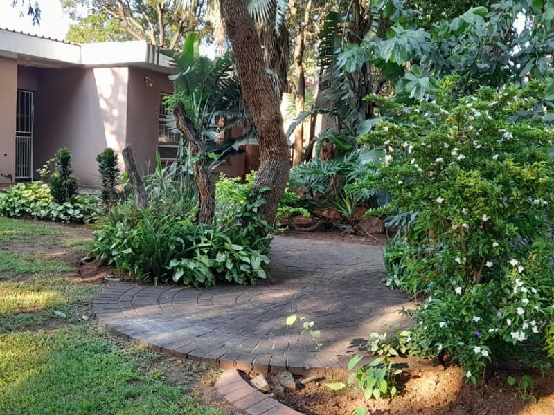 A lush, established garden featuring a circular paved pathway and mature trees, providing a serene outdoor space adjacent to the home's exterior.