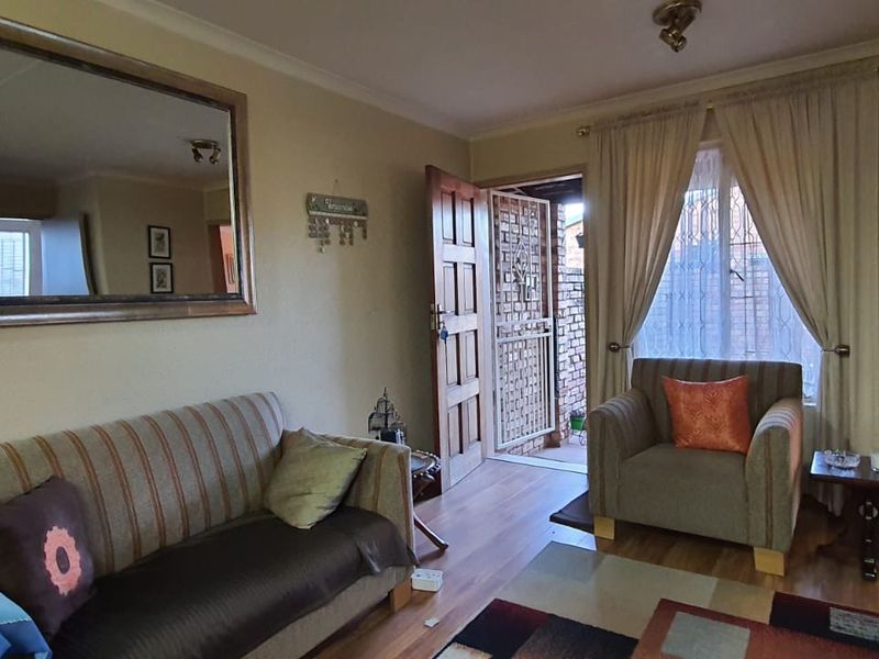 A living room featuring laminate flooring, a wooden entrance door with security gate, and access to an adjacent room.