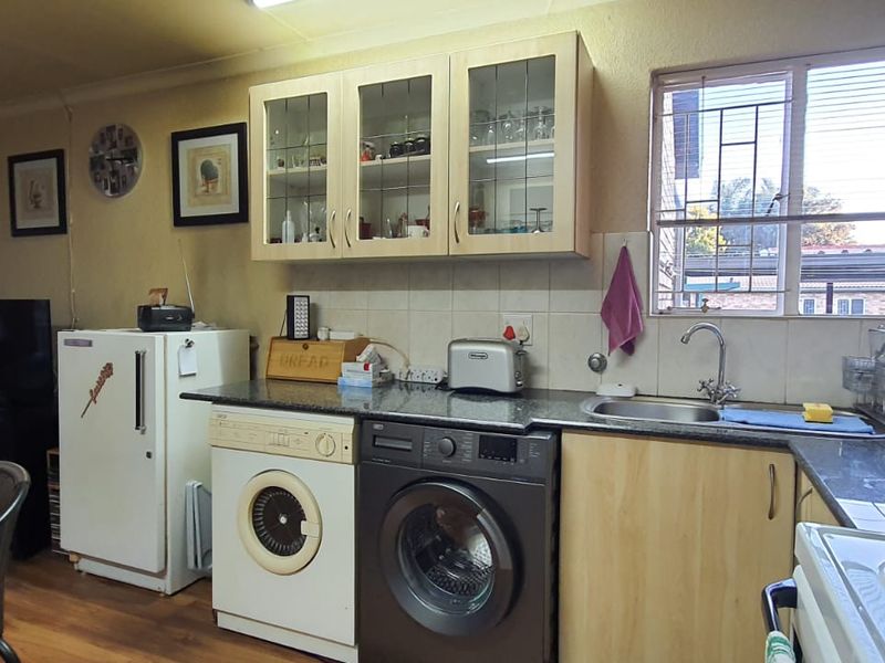 Open plan kitchen area featuring light wood cabinetry, laminate countertops, integrated laundry appliances, and a tiled splashback with a window overlooking the exterior.
