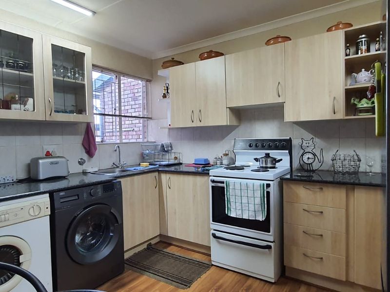 Functional kitchen featuring light wood cabinetry, granite countertops, tiled backsplash, and integrated space for laundry appliances.