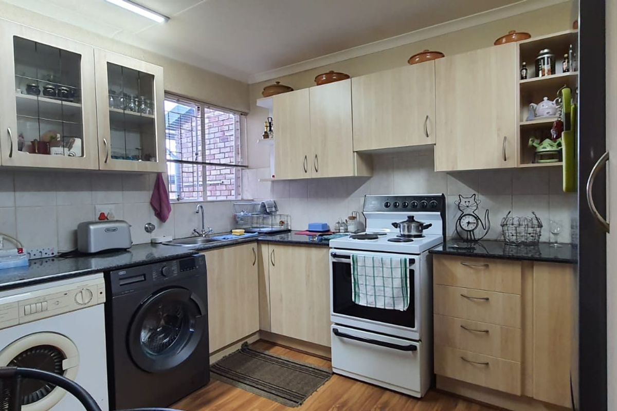 Functional kitchen featuring light wood cabinetry, granite countertops, tiled backsplash, and integrated space for laundry appliances.