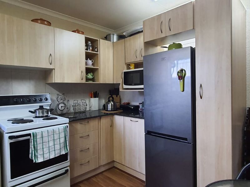 A functional kitchen featuring light wood-finish cabinetry, dark granite countertops, and a freestanding electric stove with an integrated oven.