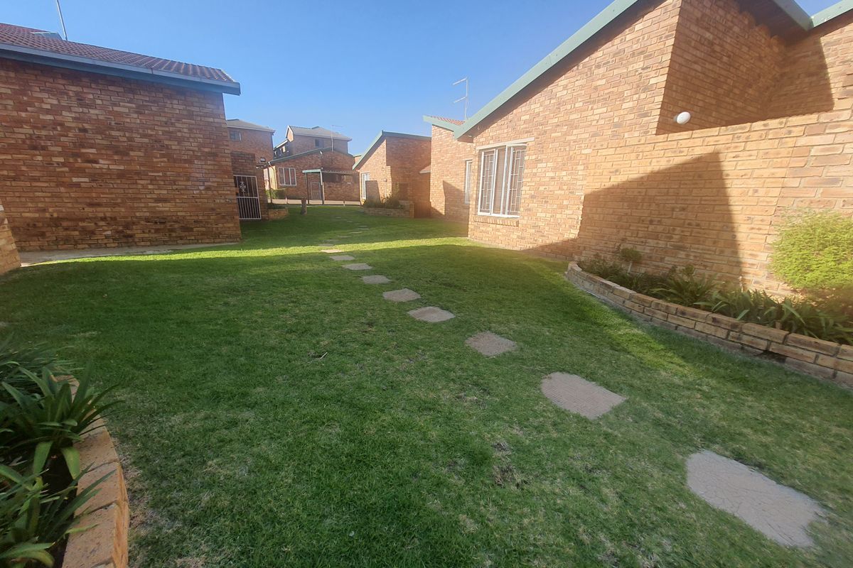 A view of the communal garden area between townhouse units, featuring brick exterior walls, a grass lawn, and stone stepping path.