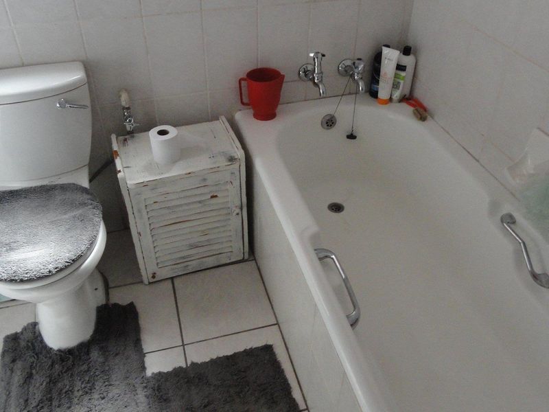 A functional bathroom featuring a standard bathtub with grab rails and a toilet, finished with white wall and floor tiles.
