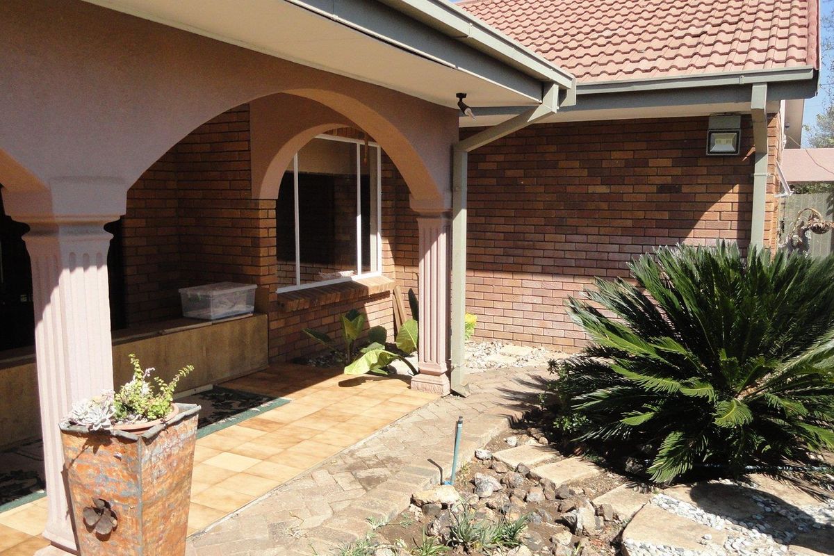 A covered patio area featuring brick walls, arched columns, and tiled flooring, providing a functional outdoor space adjacent to the main house structure.