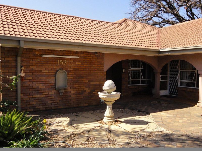 Front entrance of a brick house featuring a covered arched porch, paved courtyard area, and a decorative stone fountain.