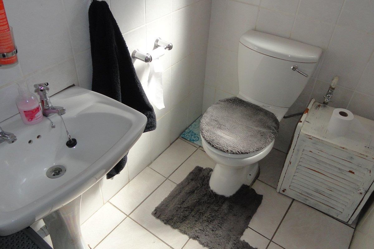 A functional bathroom featuring a white pedestal washbasin and a standard toilet with tiled walls and flooring.