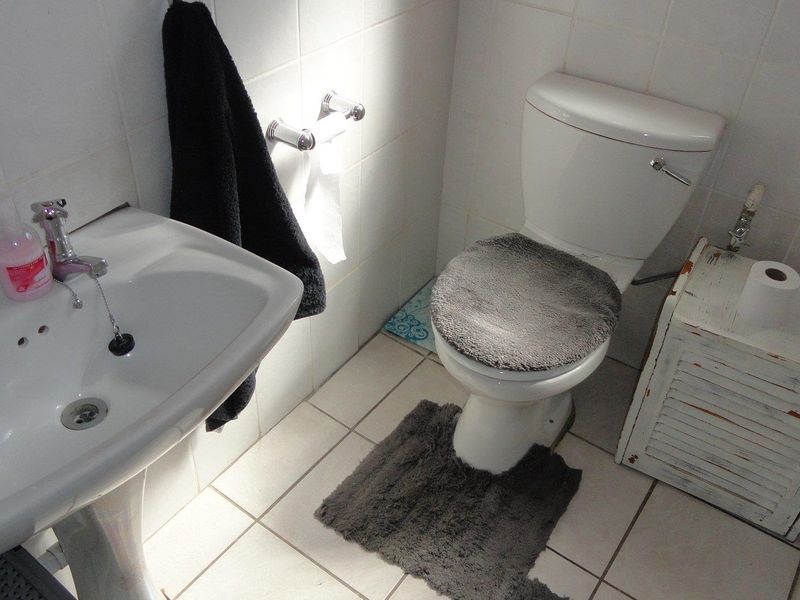 A functional bathroom featuring a white pedestal washbasin and a standard toilet with tiled walls and flooring.