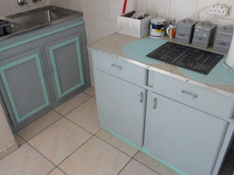 A functional scullery area featuring built-in cabinetry, a stainless steel sink, and tiled flooring, offering practical utility space for food preparation and cleaning.