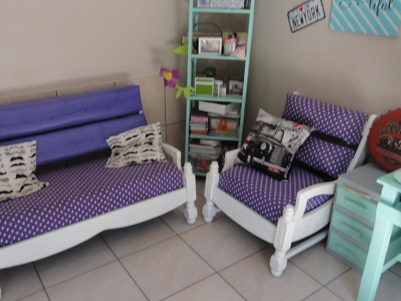A living area featuring neutral wall tones and tiled flooring, currently furnished with casual seating and storage units.