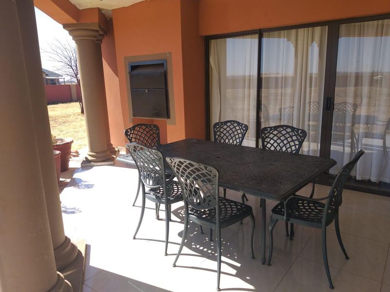 Covered patio area featuring tiled flooring, structural columns, and a built-in braai, providing direct access to the interior through sliding glass doors.