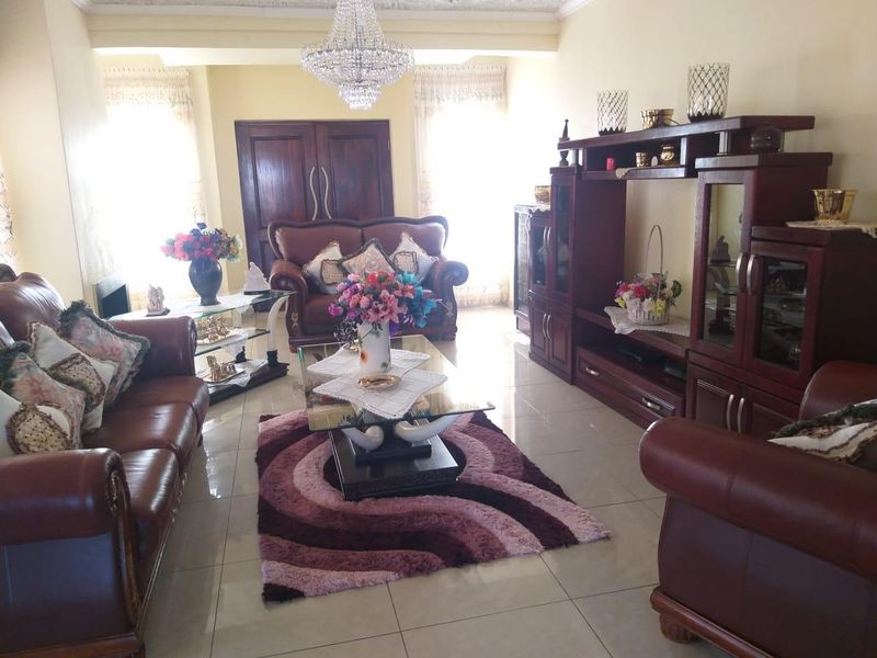 Spacious living room featuring tiled flooring, a decorative crystal chandelier, and double wooden doors, offering a traditional and comfortable living space.