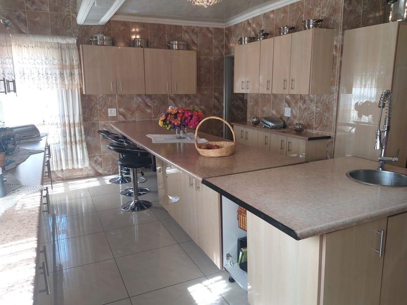 Spacious kitchen featuring light wood-finish cabinetry, extensive laminate countertops, a central island with breakfast bar seating, and full-height ceramic wall tiling.