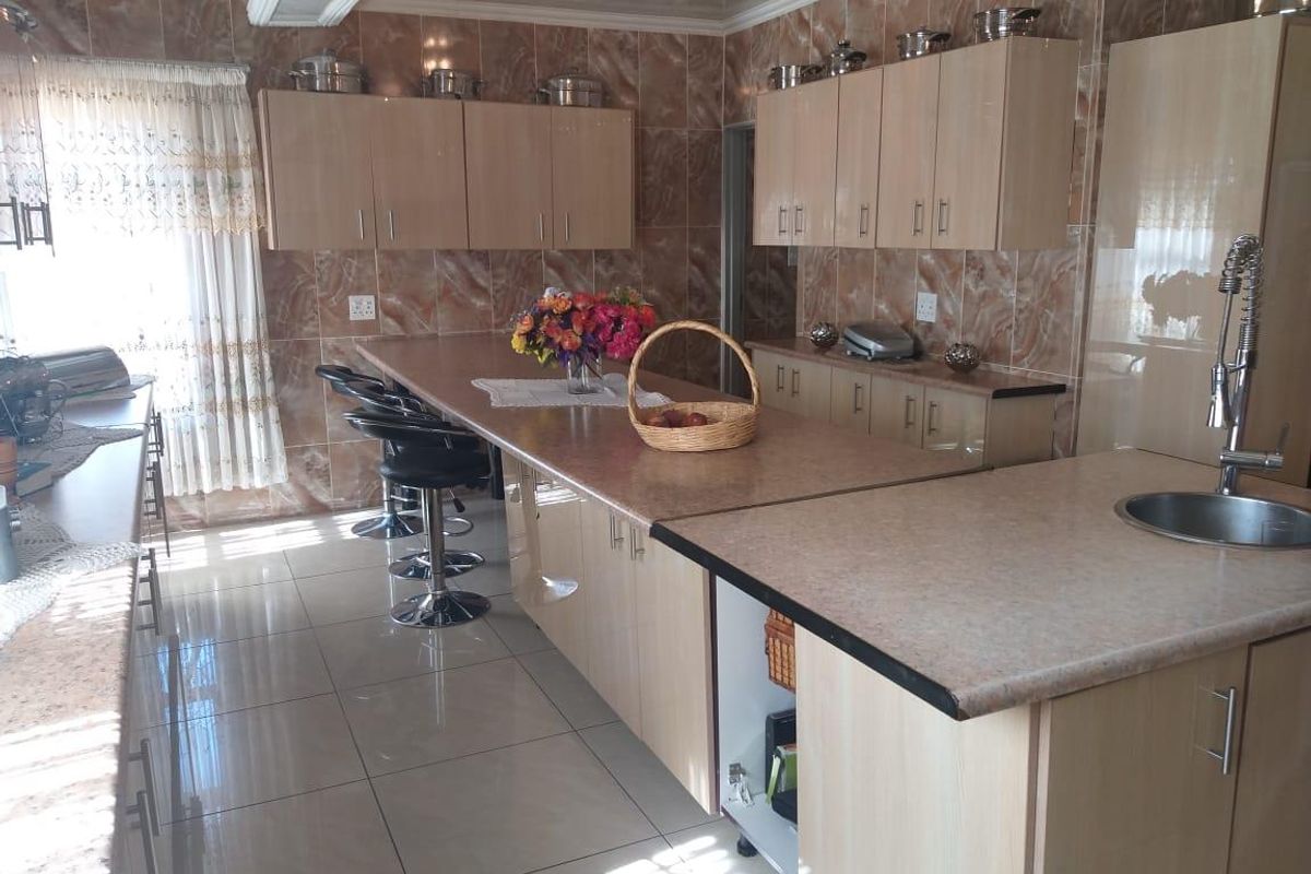 Spacious kitchen featuring light wood-finish cabinetry, extensive laminate countertops, a central island with breakfast bar seating, and full-height ceramic wall tiling.