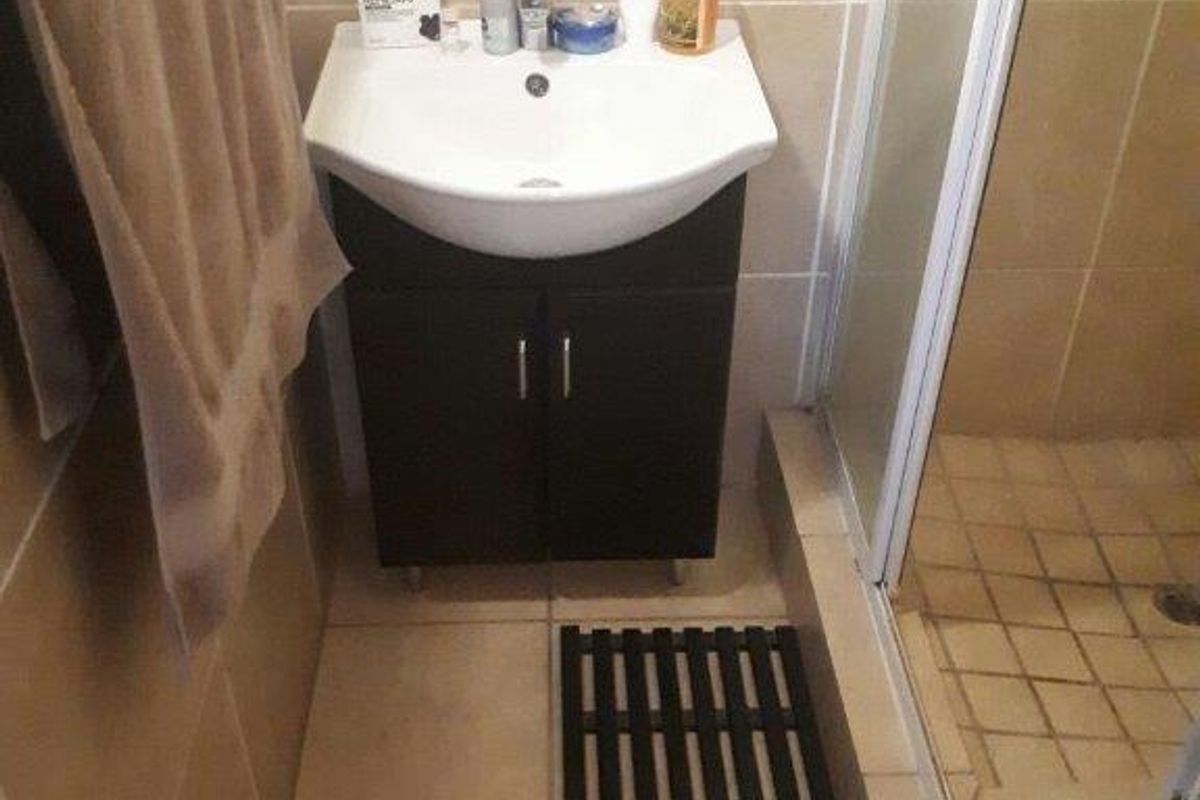 A compact bathroom featuring a wall-mounted vanity with a basin and an adjacent glass-enclosed shower stall with tiled flooring.