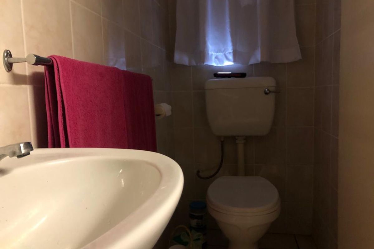A compact bathroom featuring a standard ceramic toilet and a pedestal washbasin with wall-mounted towel rail and tiled surfaces.