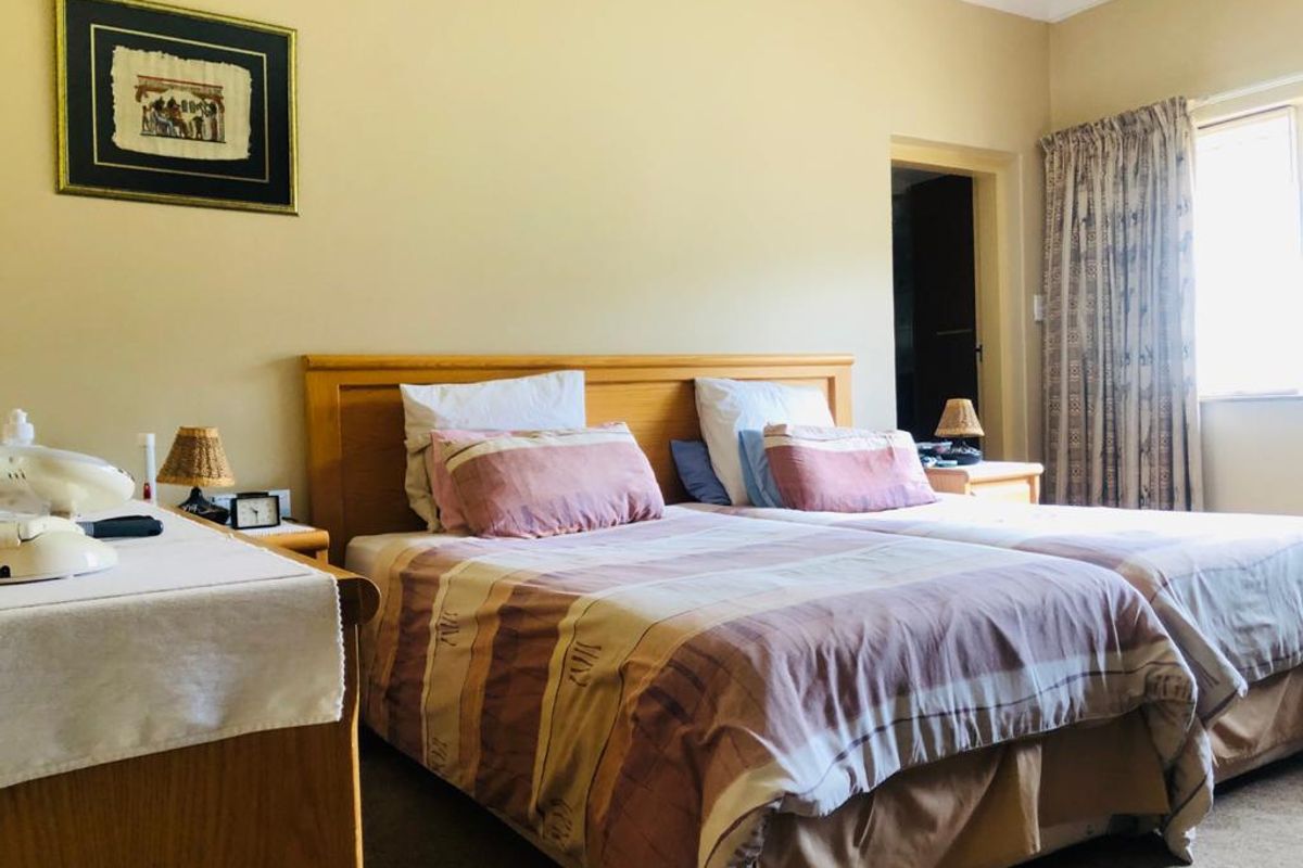 A functional bedroom featuring neutral wall tones, carpeted flooring, and a window with curtains, providing a comfortable and well-maintained living space.
