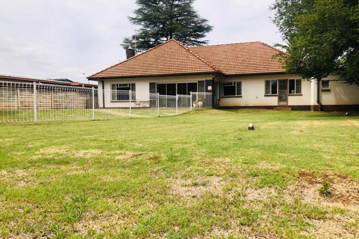 A view of the rear exterior of the house, featuring a tiled roof, white facade, and a spacious grass garden enclosed by wire fencing.