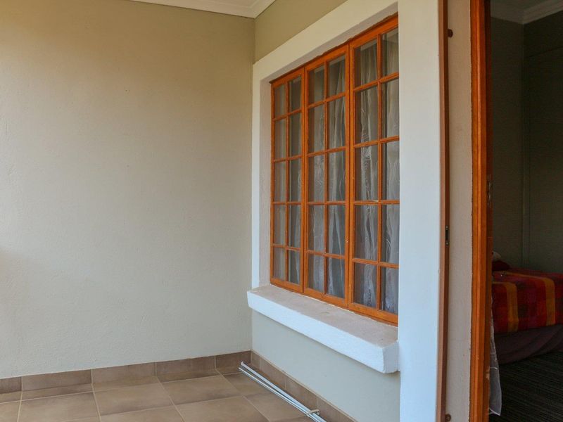 A covered balcony area featuring tiled flooring and a large wooden-framed window looking into the interior space.