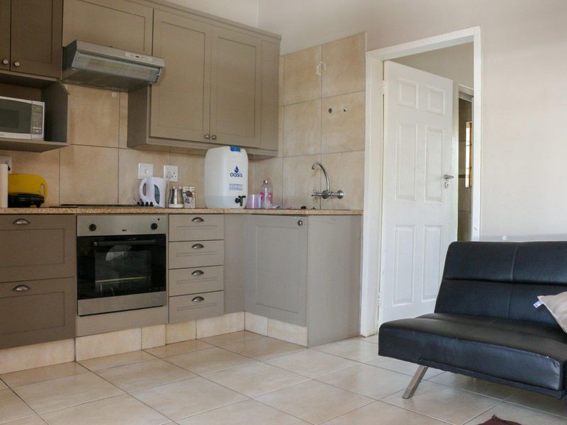 Compact open-plan kitchen featuring neutral cabinetry, built-in oven, extractor fan, and tiled flooring, seamlessly connecting to the living area.